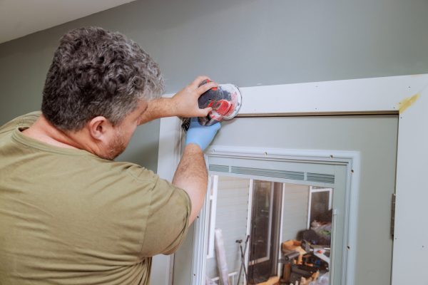 Contractor carefully sands door frame in home on refining surface for paint finish.